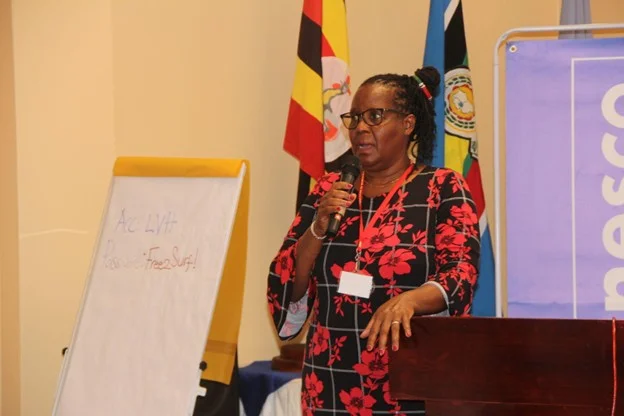 A woman speaker addresses participants beside a flip chart and flags