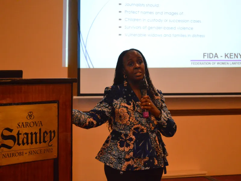 A presenter speaks to an audience beside a projected slide at a FIDA-Kenya training