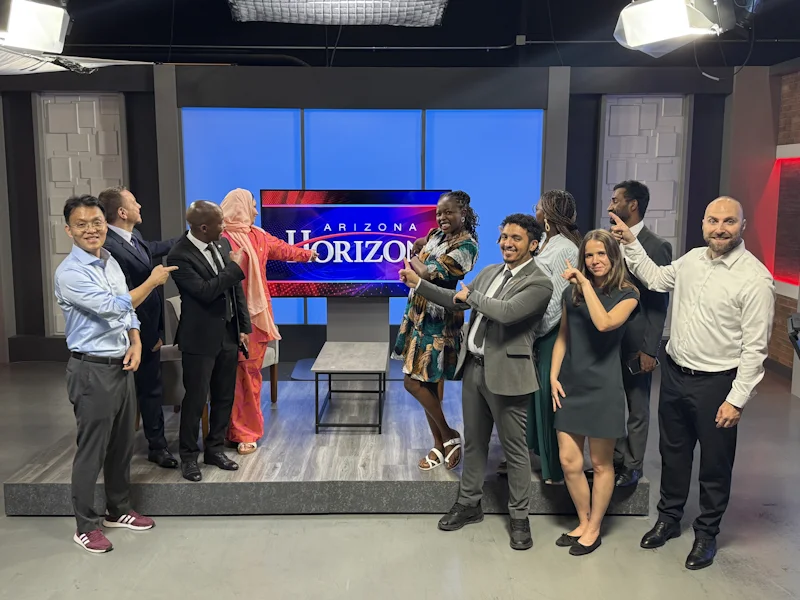 A group of fellows and hosts pose in a television studio set