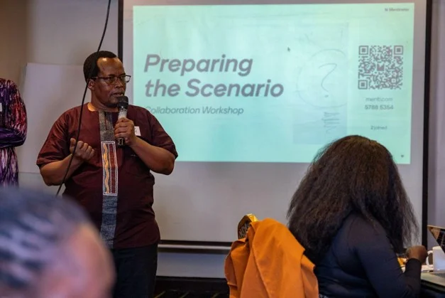 A facilitator speaks beside a slide reading “Preparing the Scenario” at a digital safety workshop